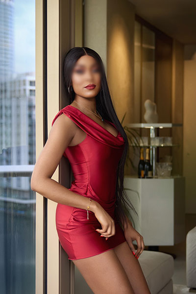 High class ebony escort in London posing next to the window in red dress.